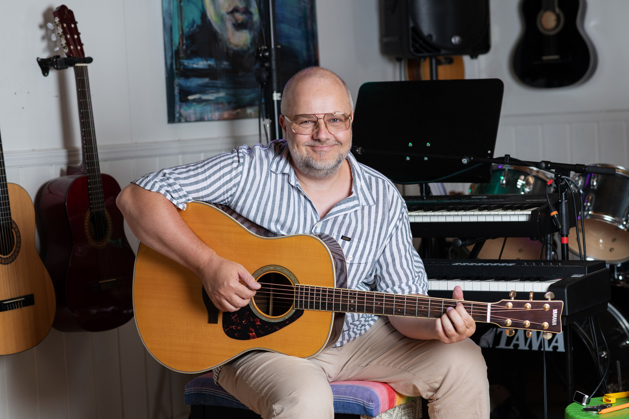 Bilde av Tommy som spiller gitar på musikkrommet med instrumenter i bakgrunnen