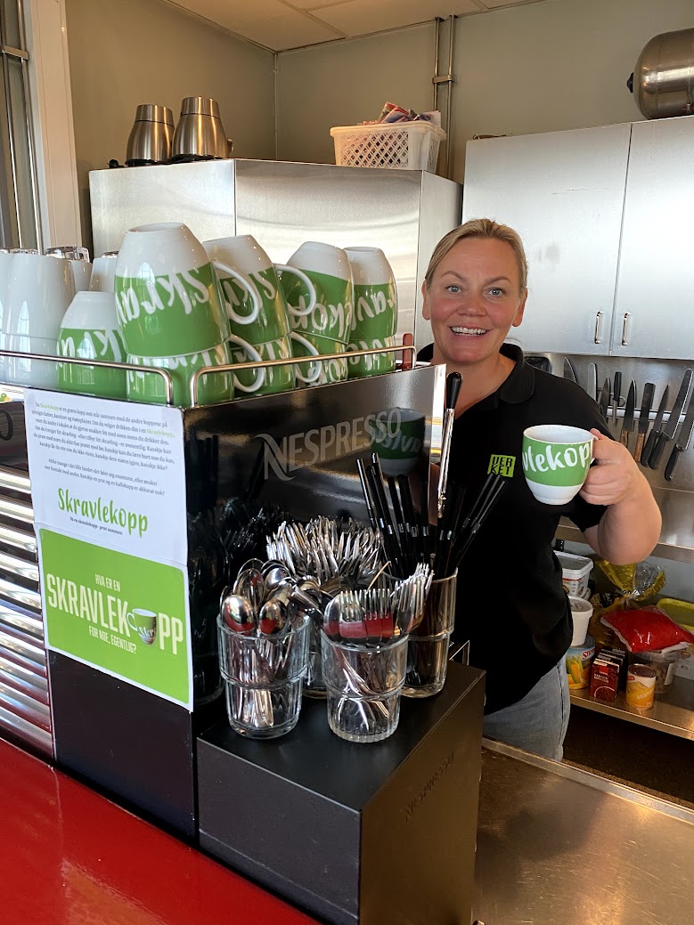 Kafemedarbeider står bak disk og serverer en kaffekopp