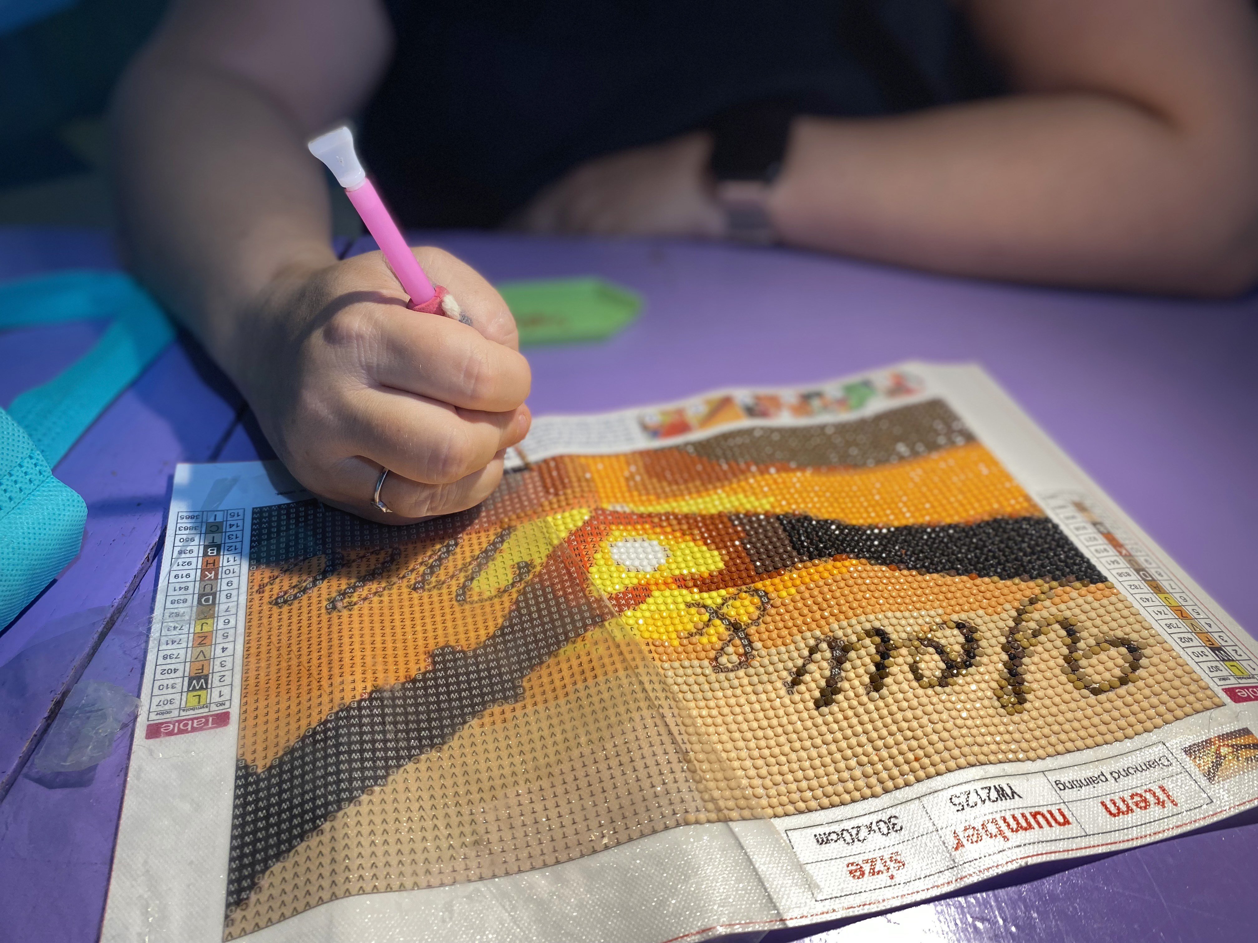 Hender som limer perler til et bilde, teknikk kalt diamond painting