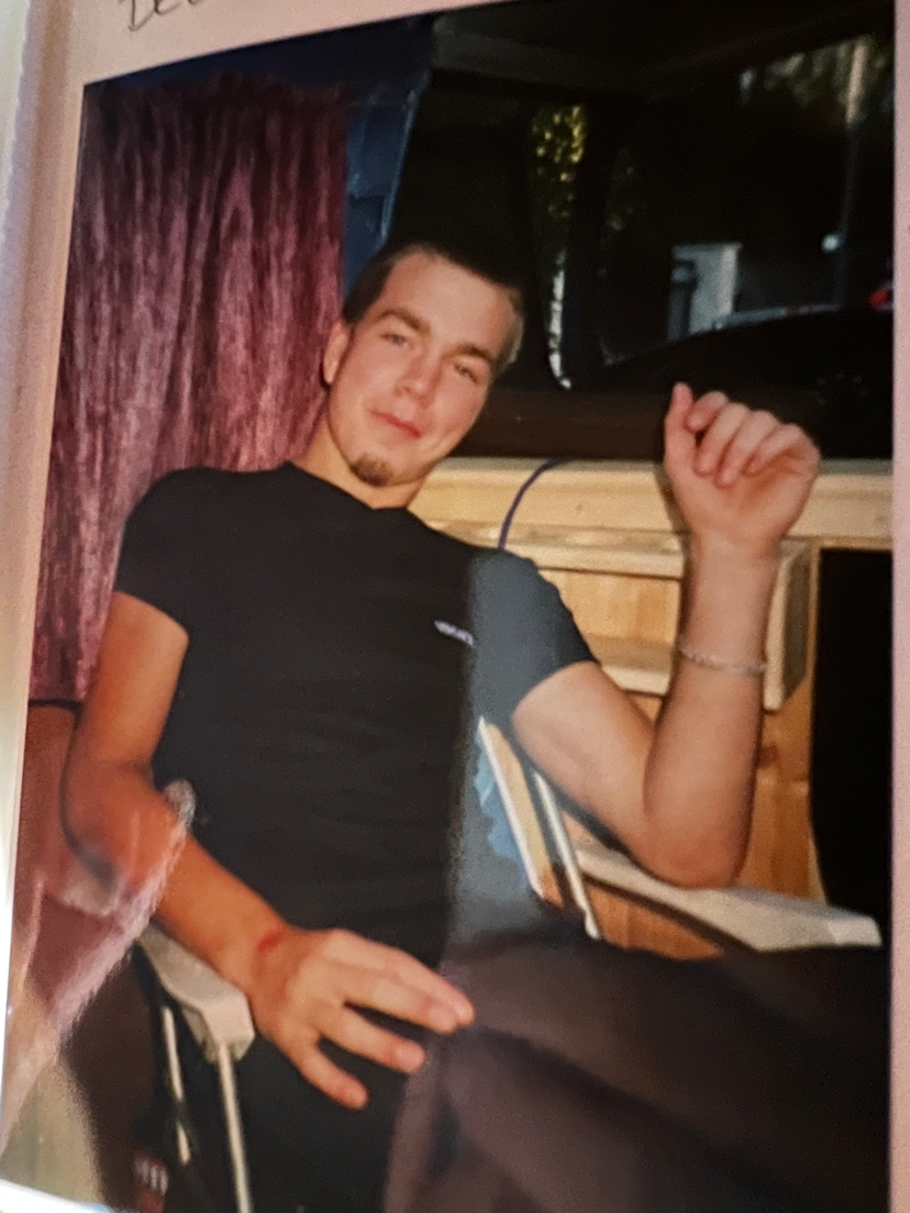 En ung mann sitter i en stol og smiler lurt til kameraet.