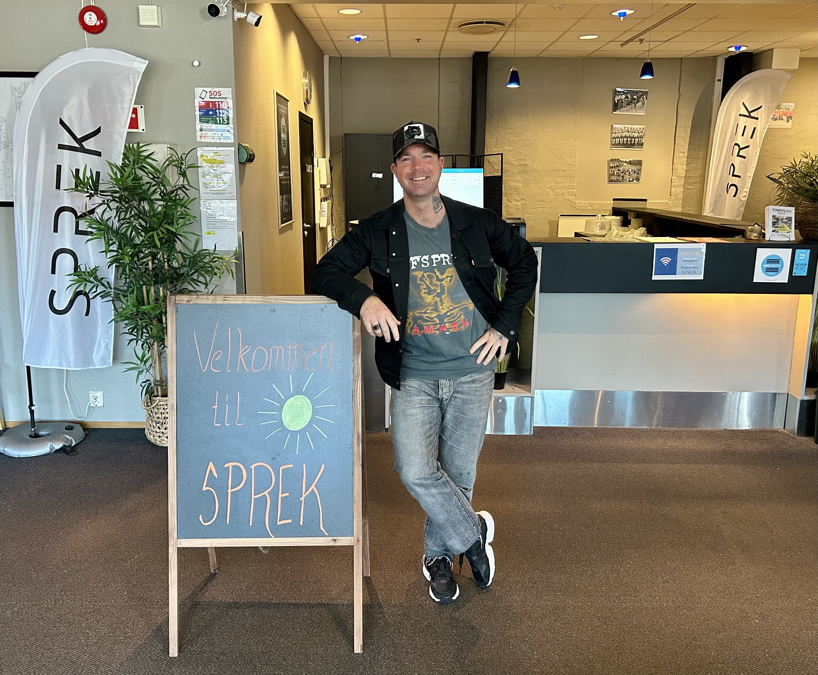 En mann lener seg på et skilt, og smiler mot kameraet.